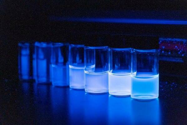 Several glass vials containing bright blue fluorescent liquid on a dark surface under blue light.